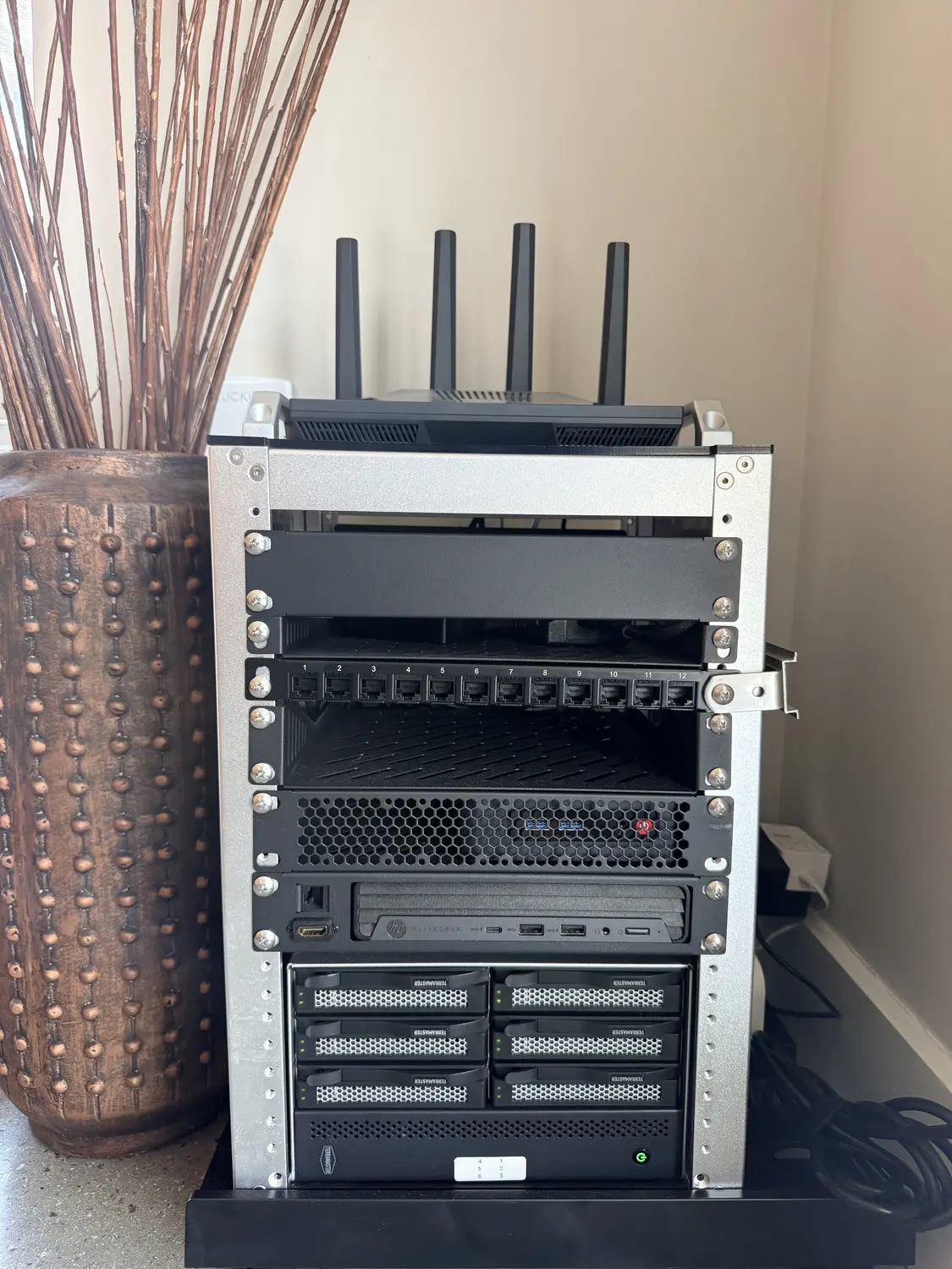 Open homelab rack — router, HP EliteDesk Mini, and a 6-bay TerraMaster DAS sitting in front of a wall arrangement